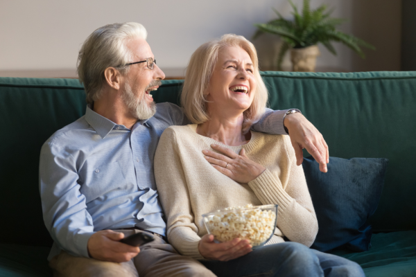 Herzlich lachendes Paar sitzt mit Popcorn vor dem Fernseher.